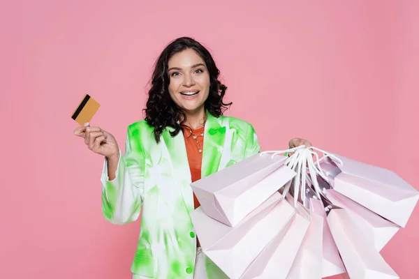 Felice giovane donna in cravatta tintura blazer in possesso di carta di credito e borse della spesa isolate su rosa — Foto stock