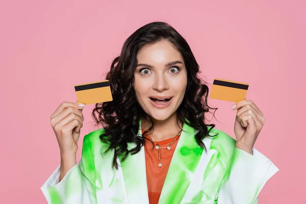 Amazed woman in green tie dye blazer holding credit cards isolated on pink — Stock Photo