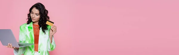 Brünette Frau im Blazer mit Kreditkarte und Laptop isoliert auf rosa Banner — Stockfoto