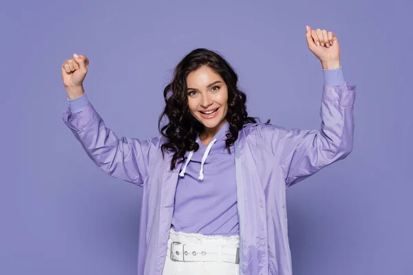 Aufgeregte junge Frau im Regenmantel mit erhobenen Händen, vereinzelt lila — Stockfoto