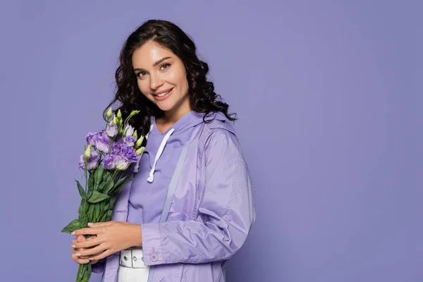 Glückliche junge Frau im Regenmantel mit Blumenstrauß auf Lila — Stockfoto