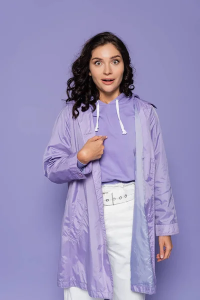 Amazed young woman in raincoat pointing at herself isolated on purple — Stock Photo