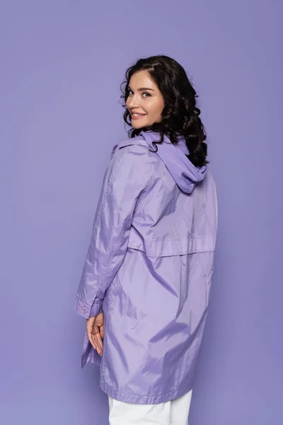 Cheerful young woman in violet raincoat isolated on purple — Stock Photo