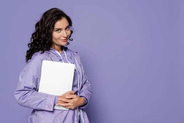 Allegra giovane donna in impermeabile viola con computer portatile isolato su viola — Foto stock