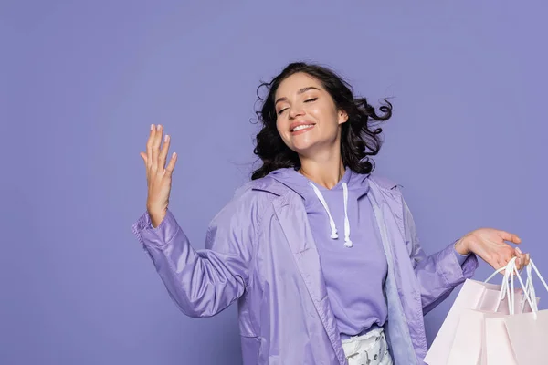 Pleased young woman with closed eyes holding shopping bags isolated on purple — Stock Photo