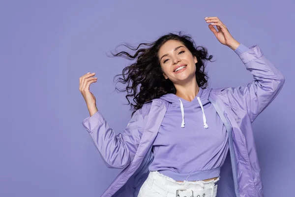 Feliz jovem mulher na capa de chuva gesticulando isolado em roxo — Fotografia de Stock