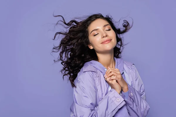 Felice giovane donna con gli occhi chiusi e le mani serrate isolate su viola — Foto stock