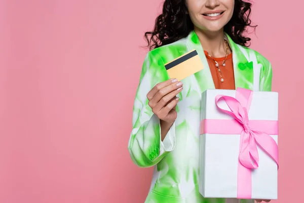 Vista recortada de la mujer alegre en corbata chaqueta de tinte con tarjeta de crédito y regalo envuelto aislado en rosa - foto de stock
