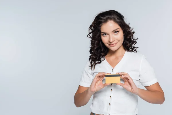 Sonriente y morena mujer sosteniendo tarjeta de crédito aislada en gris - foto de stock