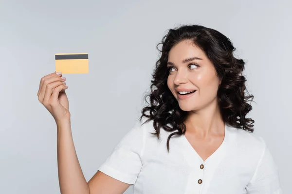 Zufriedene junge Frau schaut auf Kreditkarte isoliert auf grau — Stockfoto