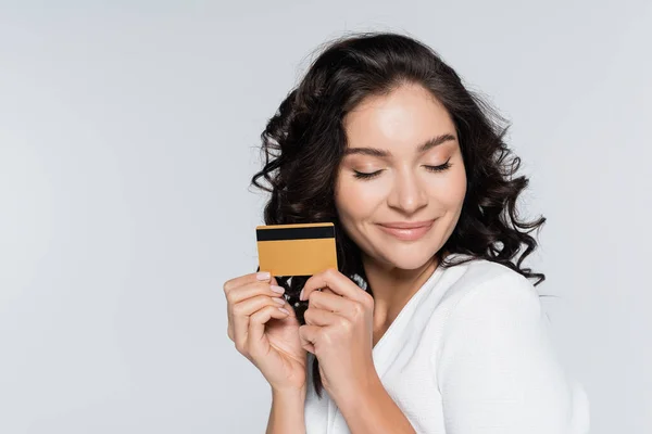 Mujer joven satisfecha sosteniendo la tarjeta de crédito aislada en gris - foto de stock