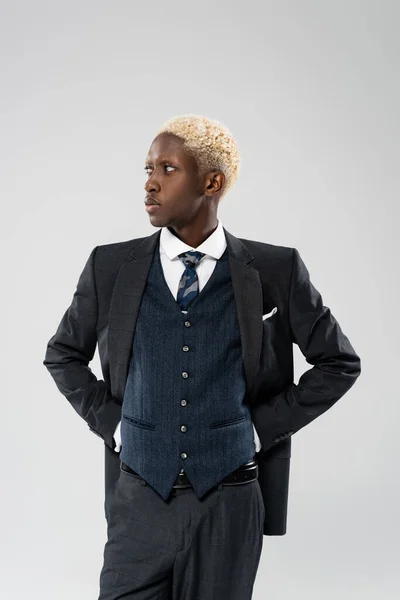 Elegante hombre de negocios afroamericano en traje posando con las manos en las caderas aisladas en gris - foto de stock