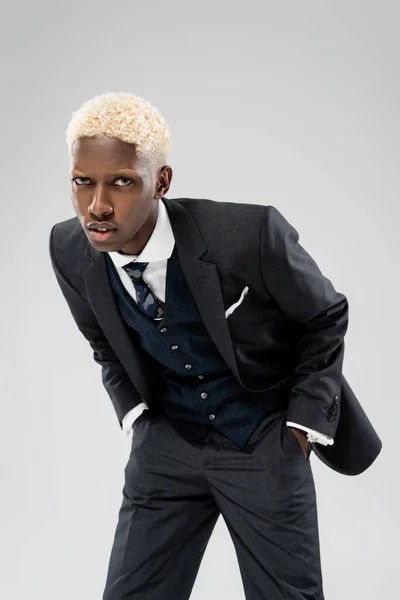 Стильний афро-американський бізнесмен в костюмі, який тримає руки в кишенях ізольованих на сірому — стокове фото