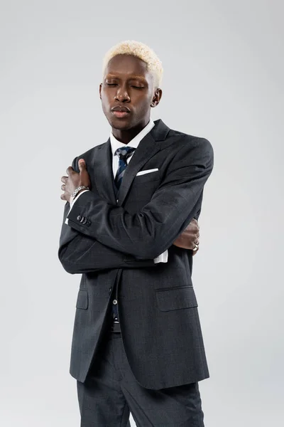 Elegante hombre de negocios afroamericano en traje posando con los brazos cruzados aislados en gris - foto de stock