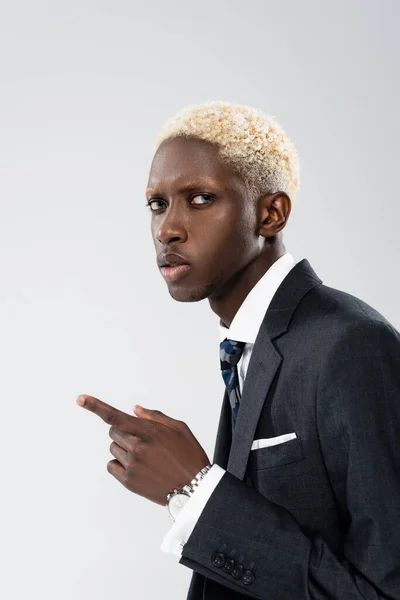 Loira e jovem empresário afro-americano de terno apontando com o dedo isolado em cinza — Fotografia de Stock