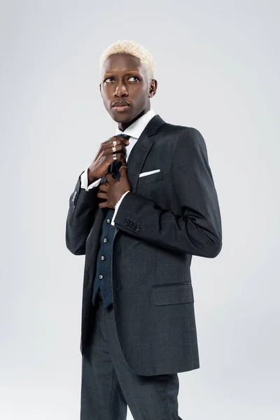 Blonde african american man in formal wear adjusting tie isolated on grey — Stock Photo