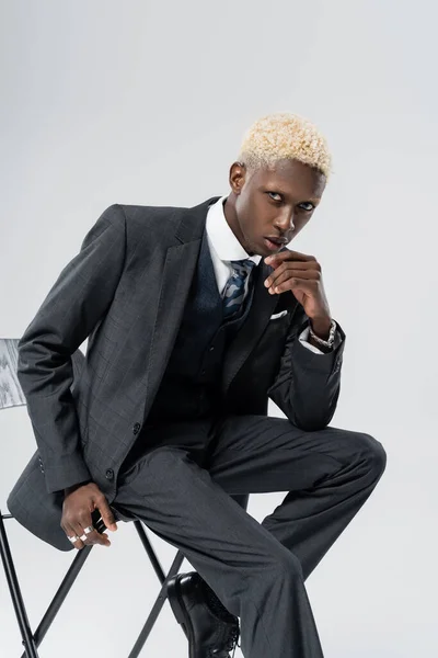 Blonde african american man in suit sitting on chair isolated on grey — Stock Photo