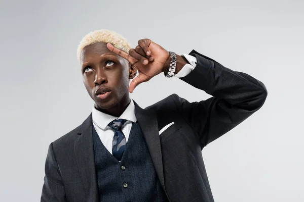 Hombre de negocios afroamericano rubio con ojos azules mirando hacia arriba y haciendo gestos aislados en gris - foto de stock