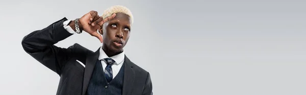 Блондин африканский американский бизнесмен с голубыми глазами, смотрящий вверх и жестикулирующий изолированно на сером, баннер — стоковое фото
