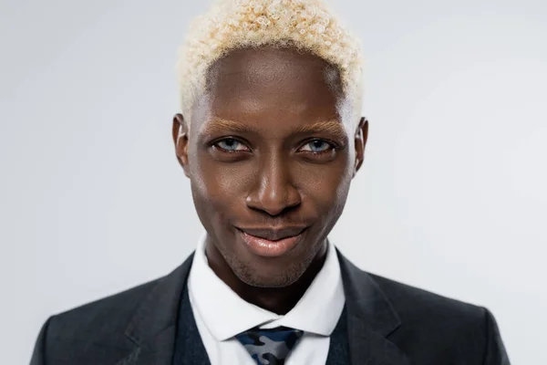 Portrait of blonde and young african american man with blue eyes smiling isolated on grey — Stock Photo