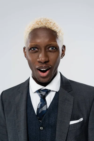 Portrait of blonde and shocked african american man with blue eyes isolated on grey — Stock Photo