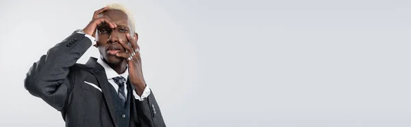 Blonder afrikanisch-amerikanischer Geschäftsmann mit blauen Augen, die das Gesicht berühren und isoliert in die Kamera auf grauem Banner schauen — Stockfoto