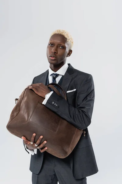 Американский блондин в костюме держит кожаную сумку, изолированную на сером — стоковое фото
