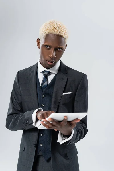 Блондинка афроамериканка в офіційному одязі тримає цифровий планшет ізольовано на сірому — стокове фото