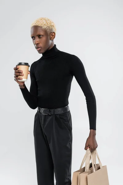 Hombre afroamericano rubio de pie con taza de papel aislado en gris - foto de stock