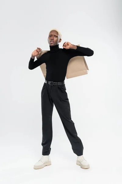 Full length of blonde african american man standing with paper bags on grey — Stock Photo