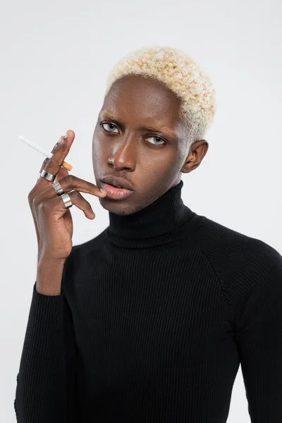 Giovane e biondo uomo afroamericano che tiene la sigaretta isolata sul grigio — Foto stock