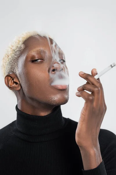 Young and blonde african american man smoking cigarette isolated on grey — Stock Photo