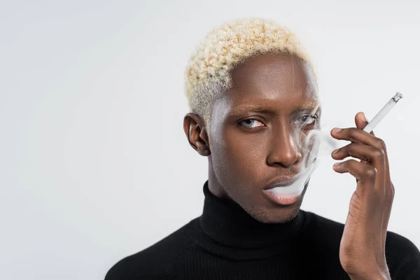 Blonde african american man with blue eyes smoking cigarette isolated on grey — Stock Photo