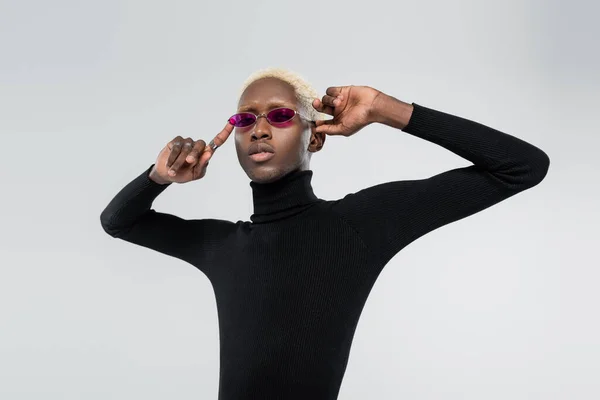 Blonde african american man in turtleneck and pink sunglasses posing isolated on grey — Stock Photo