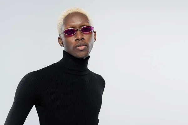 Blonder afrikanisch-amerikanischer Mann mit Rollkragen und trendiger Sonnenbrille isoliert auf grau — Stockfoto