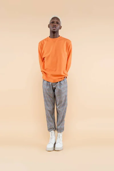 Full length of blonde african american man in orange sweatshirt posing on beige — Stock Photo