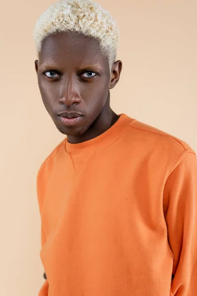 Blonde african american man in orange sweatshirt looking at camera isolated on beige — Stock Photo