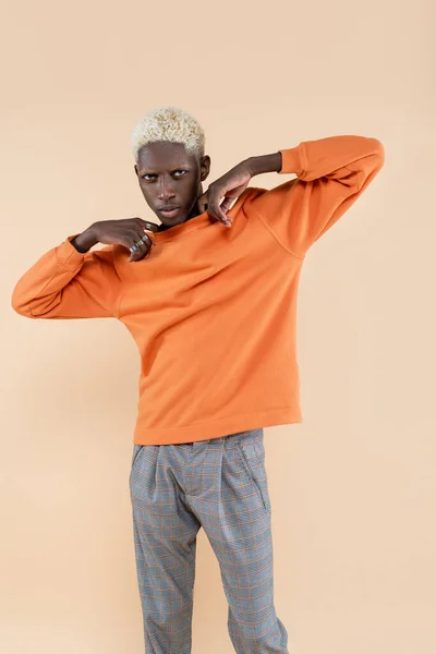 Joven afroamericano hombre en sudadera naranja mirando cámara aislada en beige - foto de stock