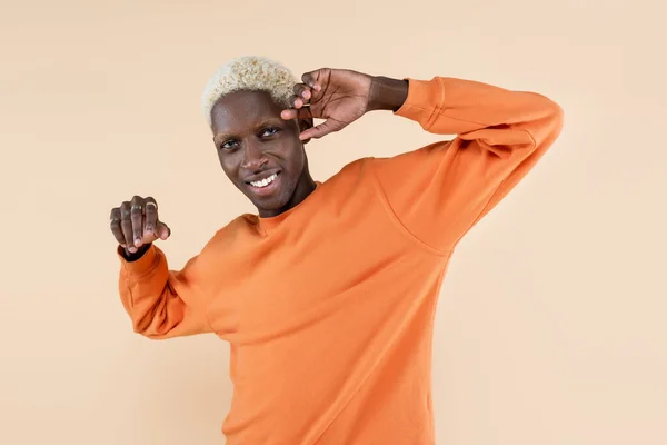 Happy african american man in orange sweatshirt looking at camera isolated on beige — Stock Photo