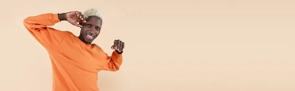 Glücklicher afrikanisch-amerikanischer Mann in orangefarbenem Sweatshirt, der isoliert auf beige gehaltene Kamera blickt, Banner — Stockfoto