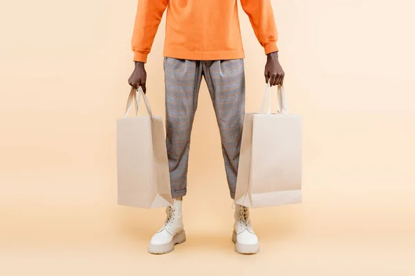 Vista cortada do homem americano africano em camisola laranja segurando sacos de compras no bege — Fotografia de Stock