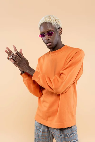 Jovem afro-americano em óculos de sol rosa e camisola posando isolado no bege — Fotografia de Stock