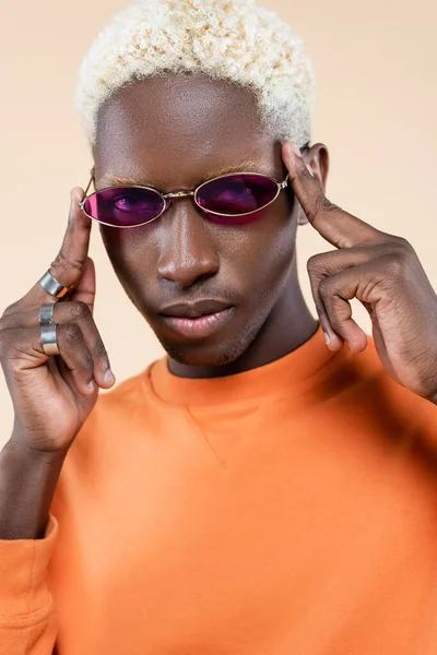 Retrato de un joven afroamericano en gafas de sol rosas y sudadera aislada en beige - foto de stock