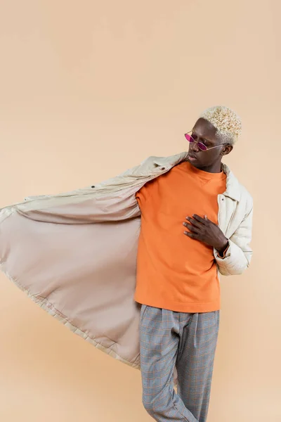 Jeune homme afro-américain dans des lunettes de soleil élégantes et manteau isolé sur beige — Photo de stock