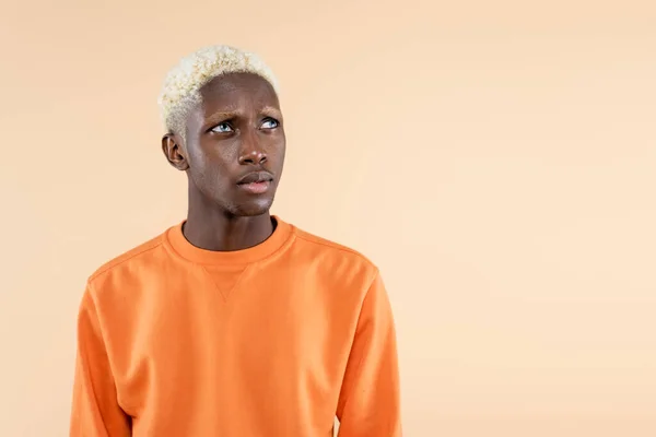 Dreamy african american man in orange sweatshirt looking away isolated on beige — Stock Photo