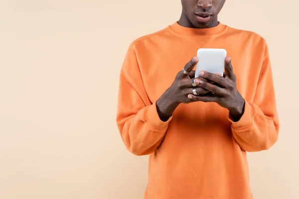 Vista recortada del hombre afroamericano en sudadera naranja usando smartphone aislado en beige - foto de stock