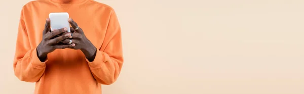 Cropped view of african american man in orange sweatshirt using smartphone isolated on beige, banner — Stock Photo