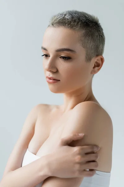 Молода жінка з коротким волоссям і голими плечима обіймає себе ізольовано на сірому — стокове фото