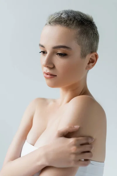 Young woman with short hair and bare shoulders hugging herself isolated on grey — Stock Photo