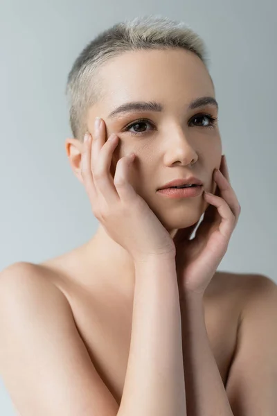 Vista de cerca de la mujer sensual con maquillaje natural tocando la cara aislado en gris - foto de stock